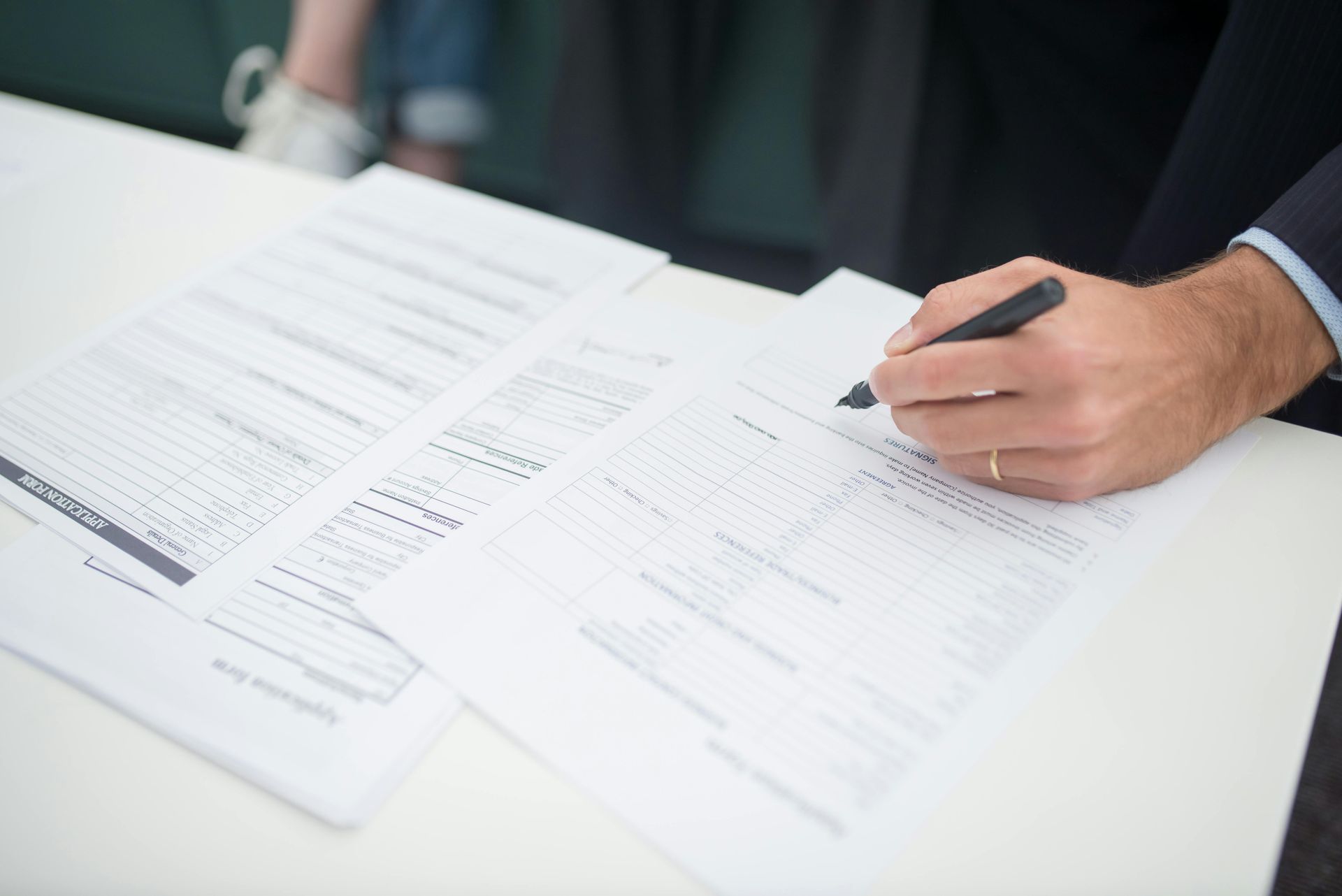 A man is sitting at a table signing a document with a pen.