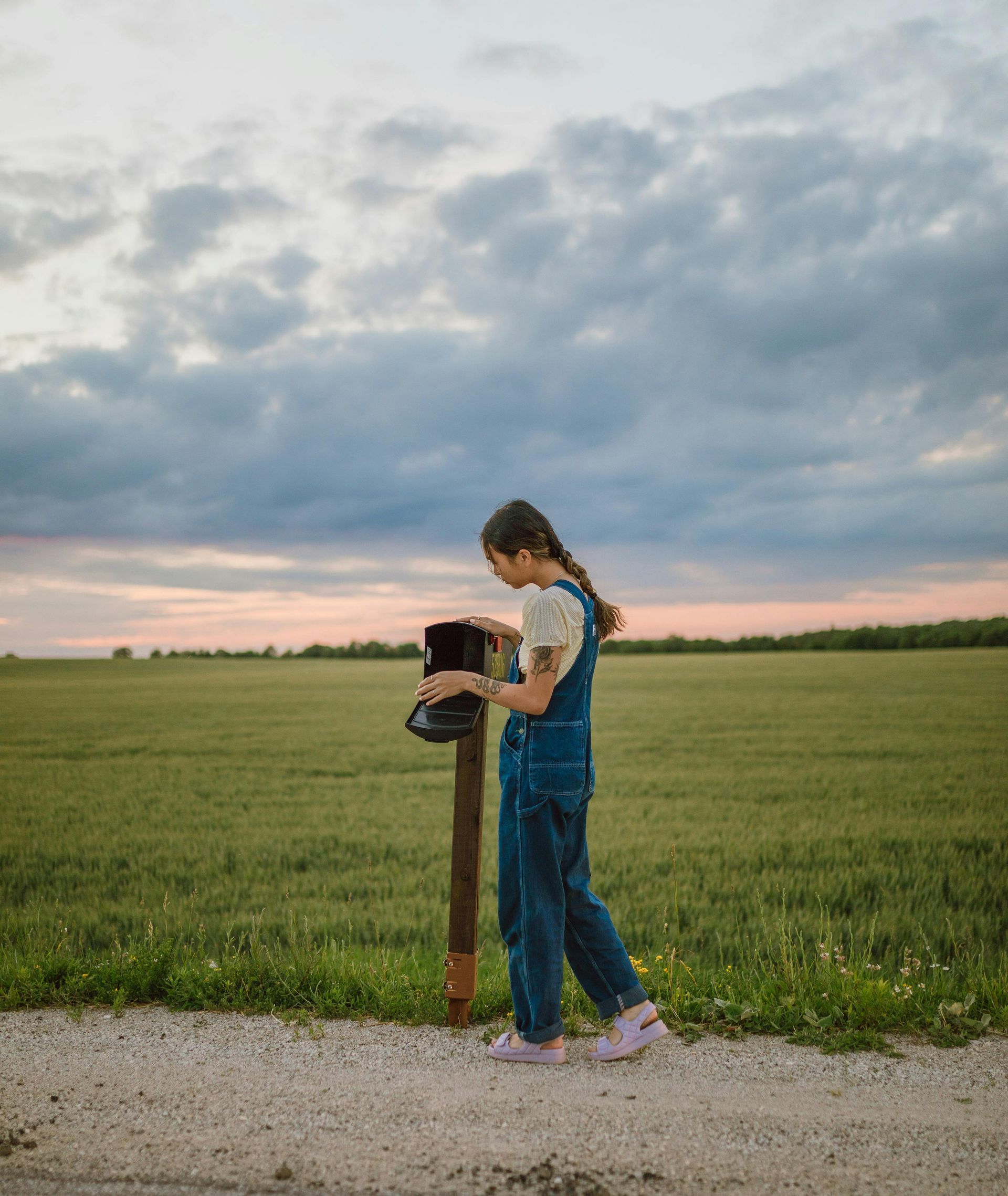 A woman is standing next to a mailbox in a field.