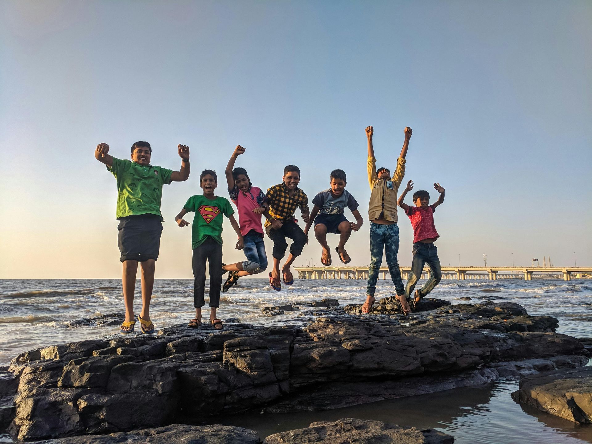 A group of children are jumping in the air on a rocky beach.
