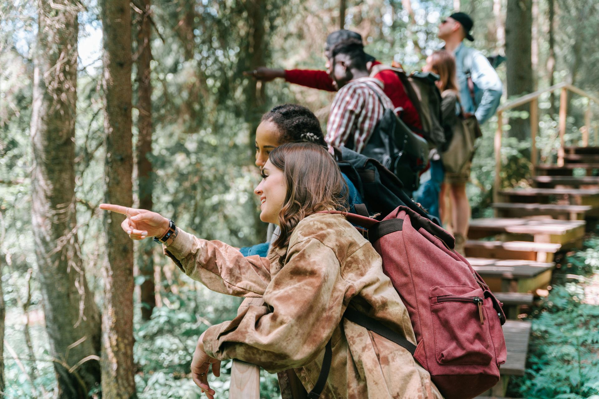 A group of people are hiking in the woods and one of them is pointing at something.