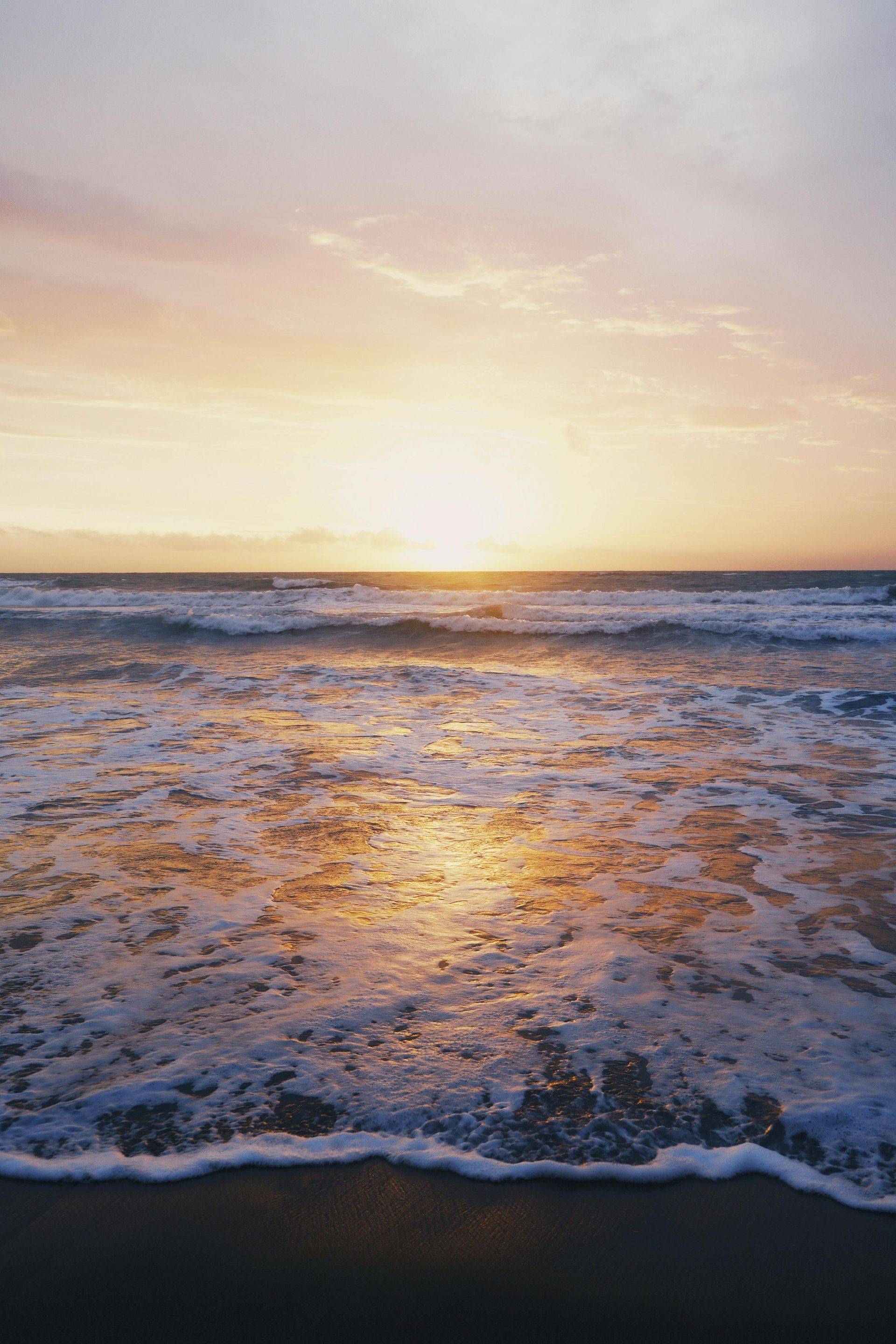 The sun is setting over the ocean and the waves are crashing on the beach.