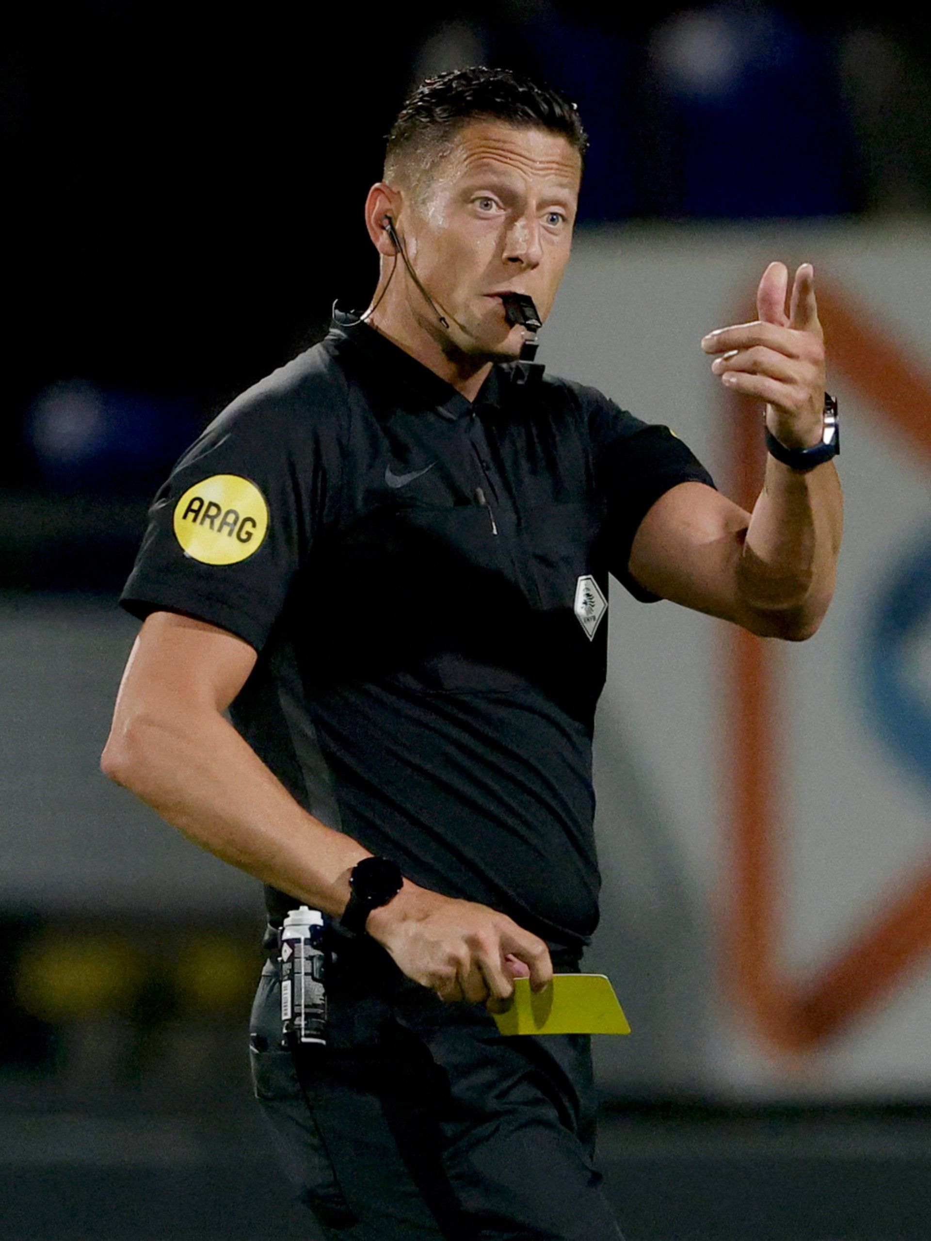Een voetbalarbitrator houdt een gele kaart vast en geeft met zijn hand een signaal.