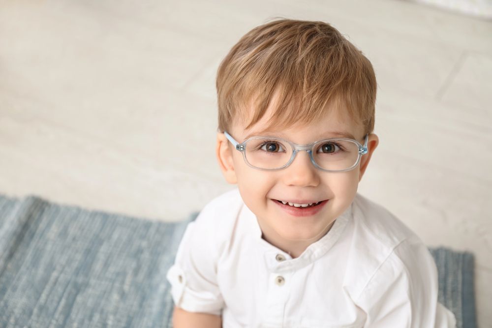 Un ragazzo con gli occhiali sorride, seduto su un tappeto blu e con indosso una camicia bianca.
