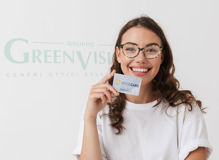 Donna sorridente con in mano un biglietto da visita e occhiali, davanti al logo di Green Vision.
