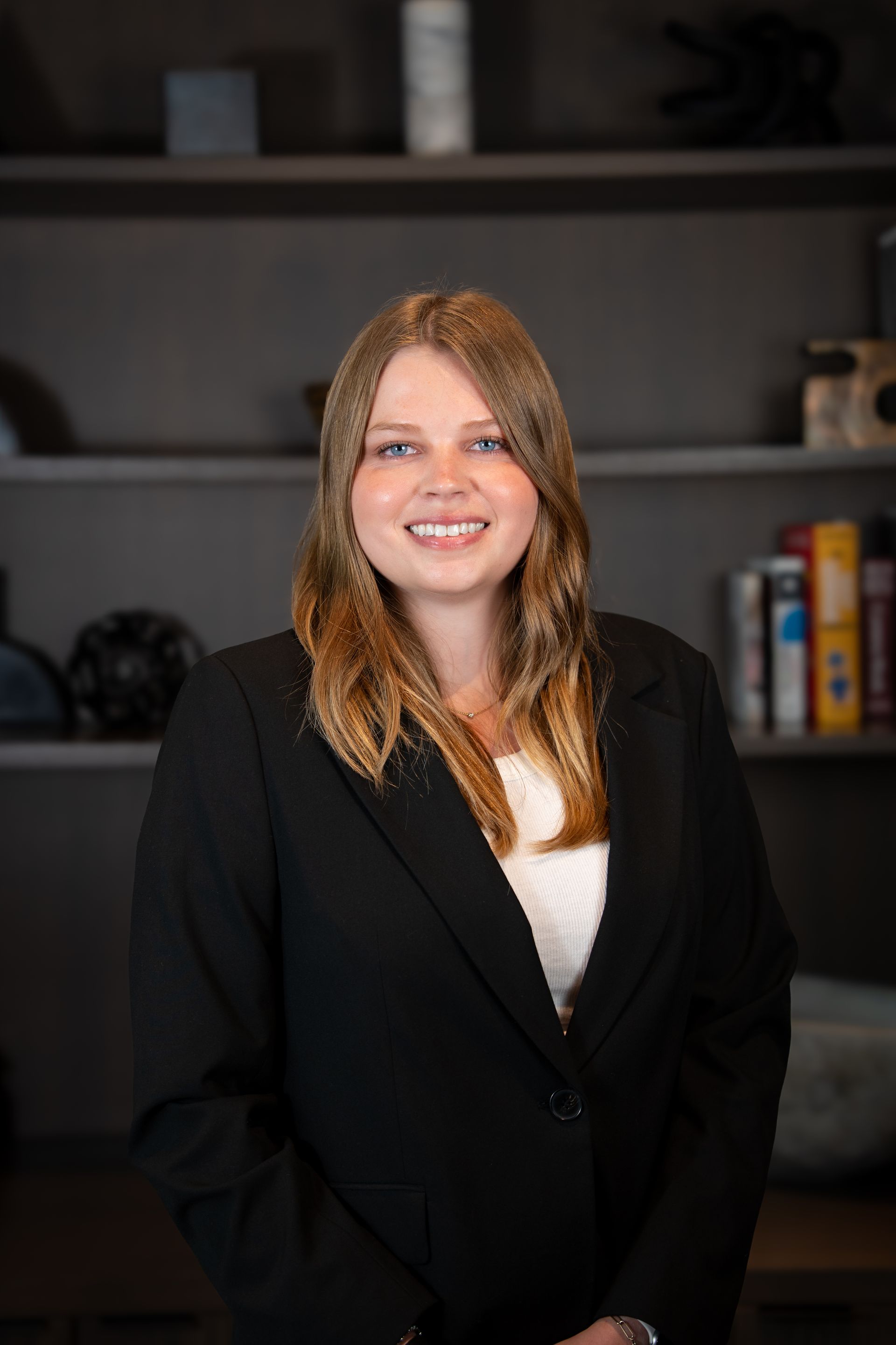 Woman in a black blazer smiling in front of a bookshelf.