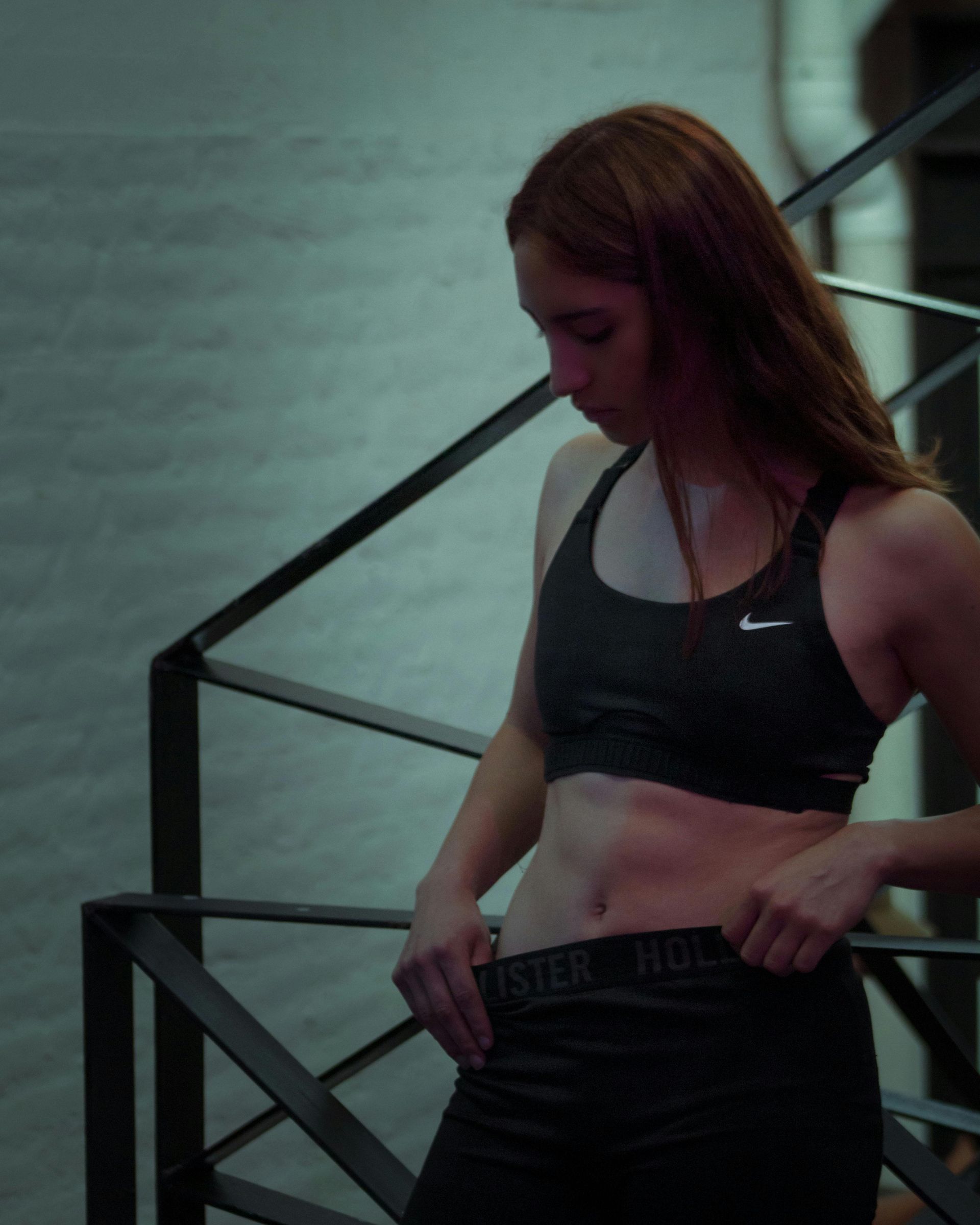 Mujer en sujetador deportivo y mallas, se detiene en las escaleras, mira hacia abajo.