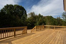 A large wooden deck with a railing and trees in the background