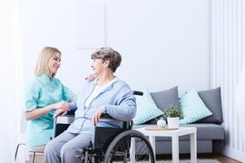 home health aide kneeling beside woman in wheelchair
