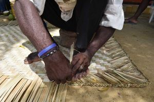 Un hombre está haciendo una estera con palos de bambú.