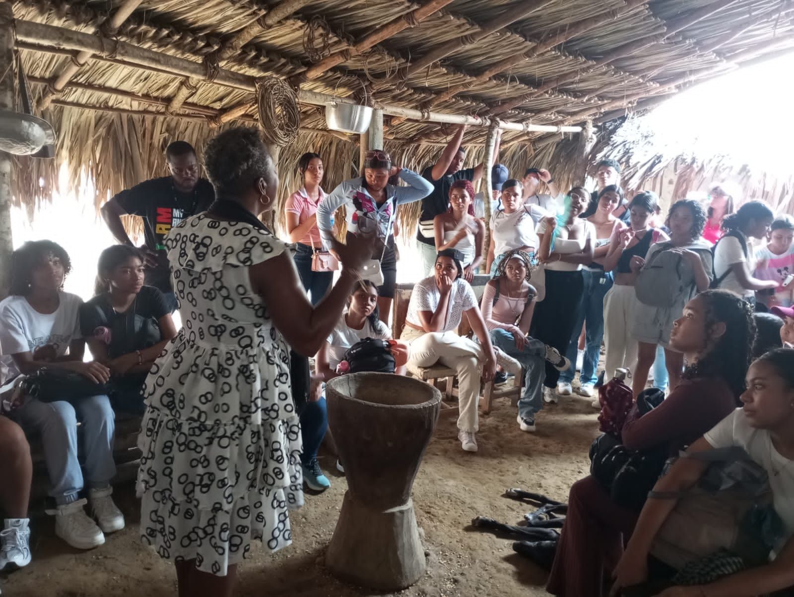 Una mujer está parada frente a un tambor hablando con un grupo de personas.