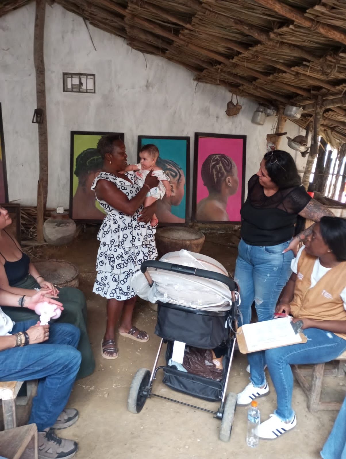 Un grupo de personas sentadas alrededor de un cochecito y una mujer sosteniendo un bebé.