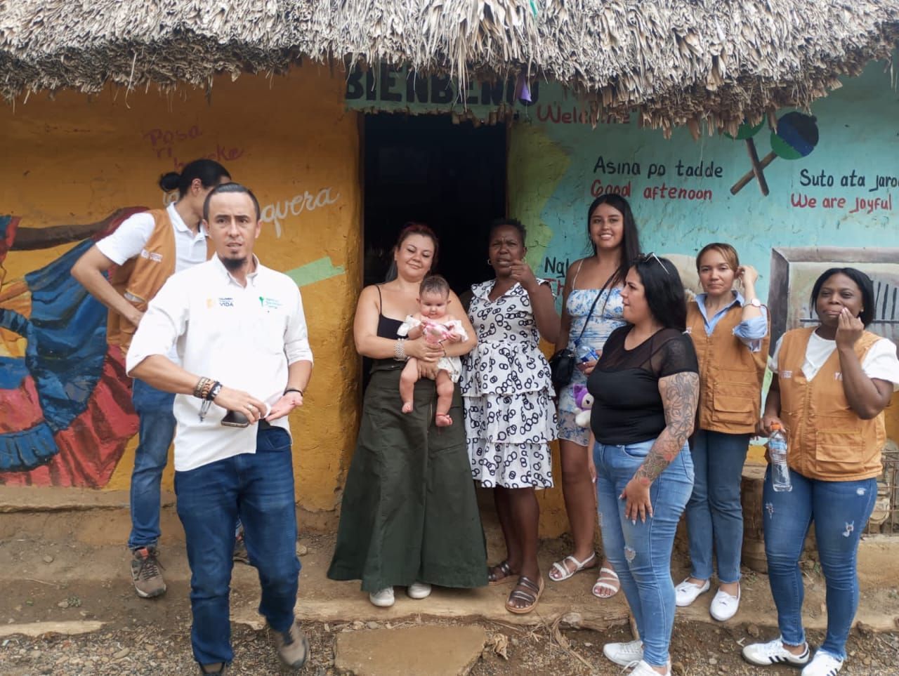 Un grupo de personas está de pie frente a un edificio con techo de paja.