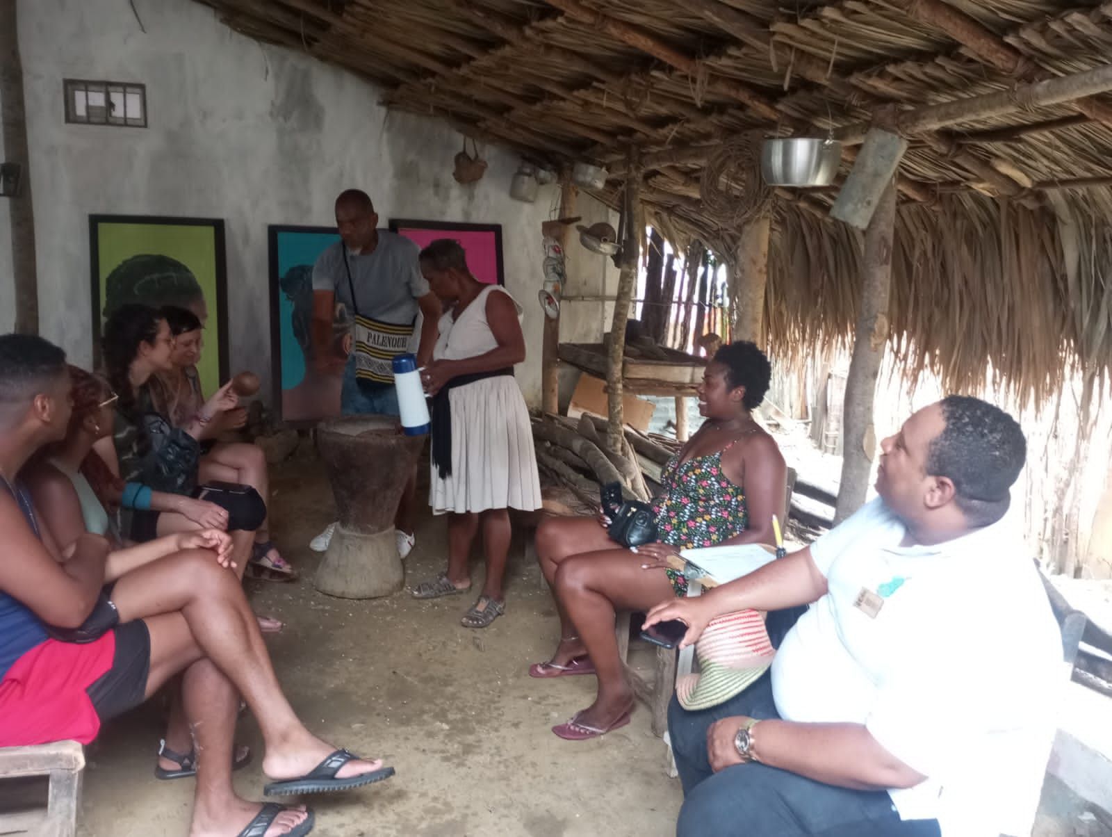 Un grupo de personas está sentado en una choza bajo un techo de paja.