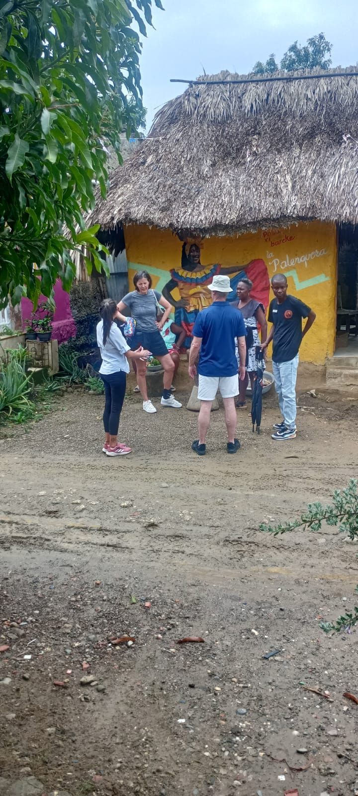 Un grupo de personas está de pie frente a un edificio amarillo con techo de paja.