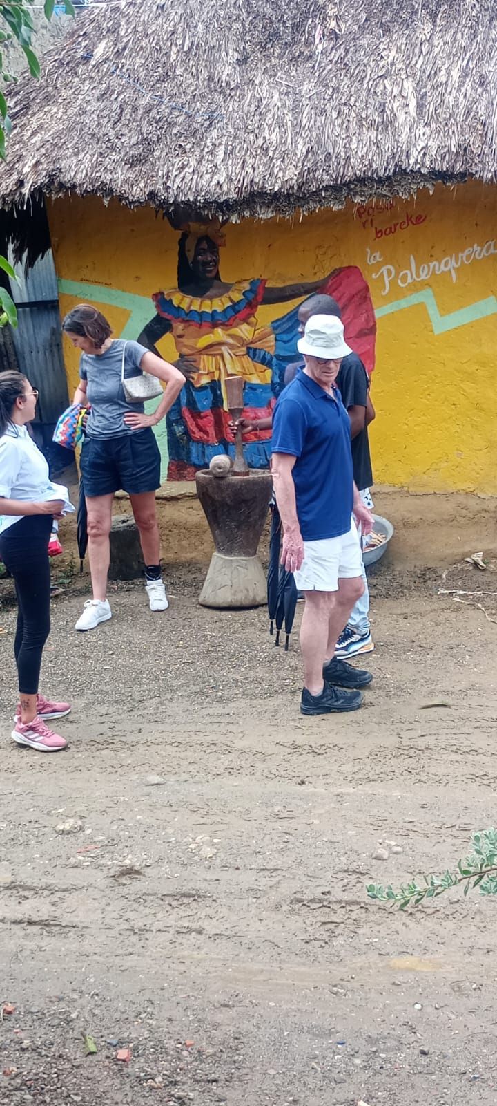Un grupo de personas está de pie frente a un edificio amarillo con techo de paja.