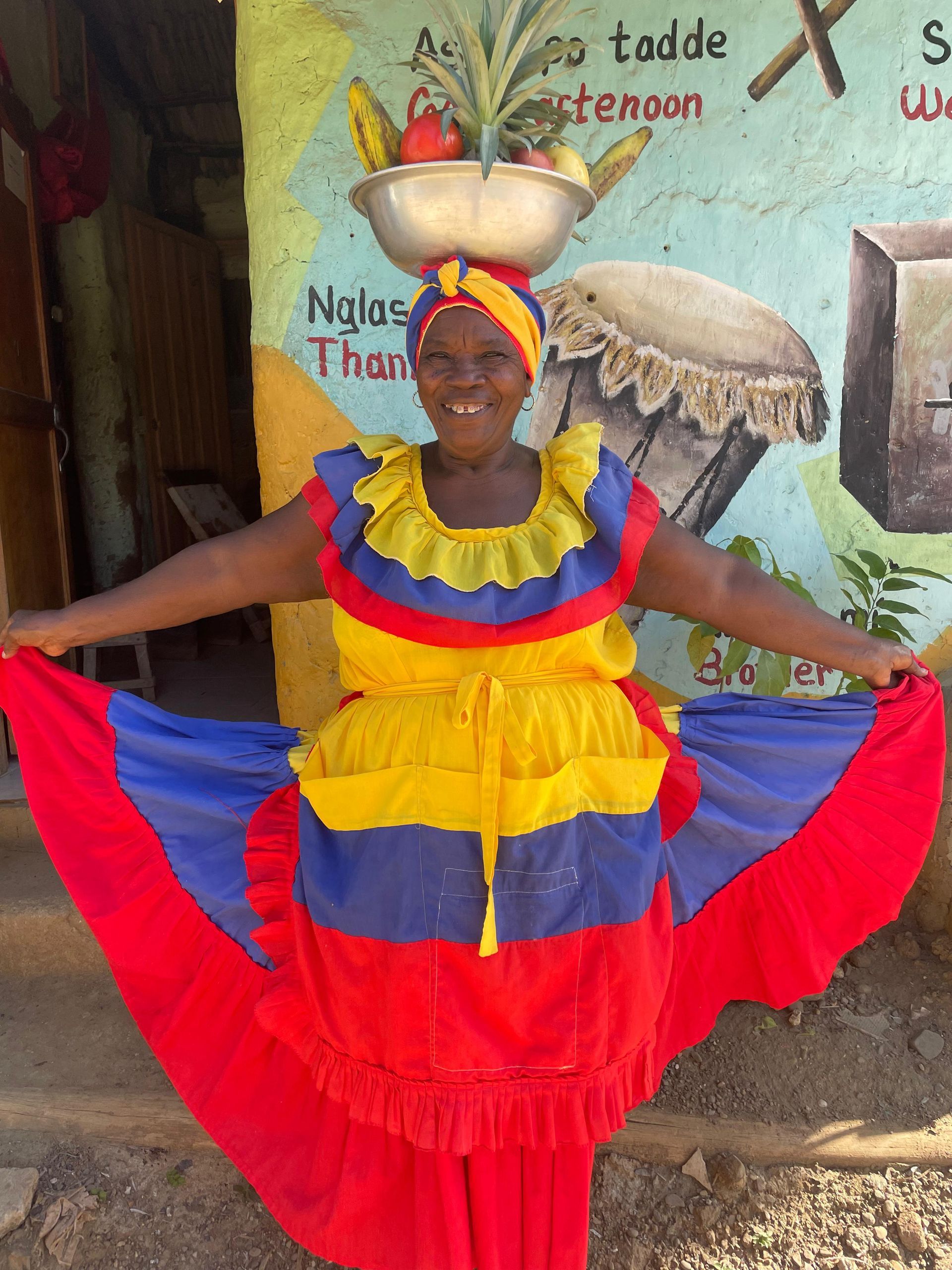 Una mujer con un vestido colorido tiene un bol de fruta en la cabeza.