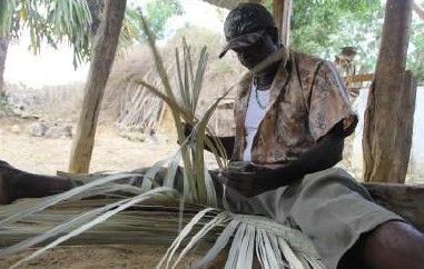 Un hombre está sentado en el suelo haciendo una cesta con hojas de palma.