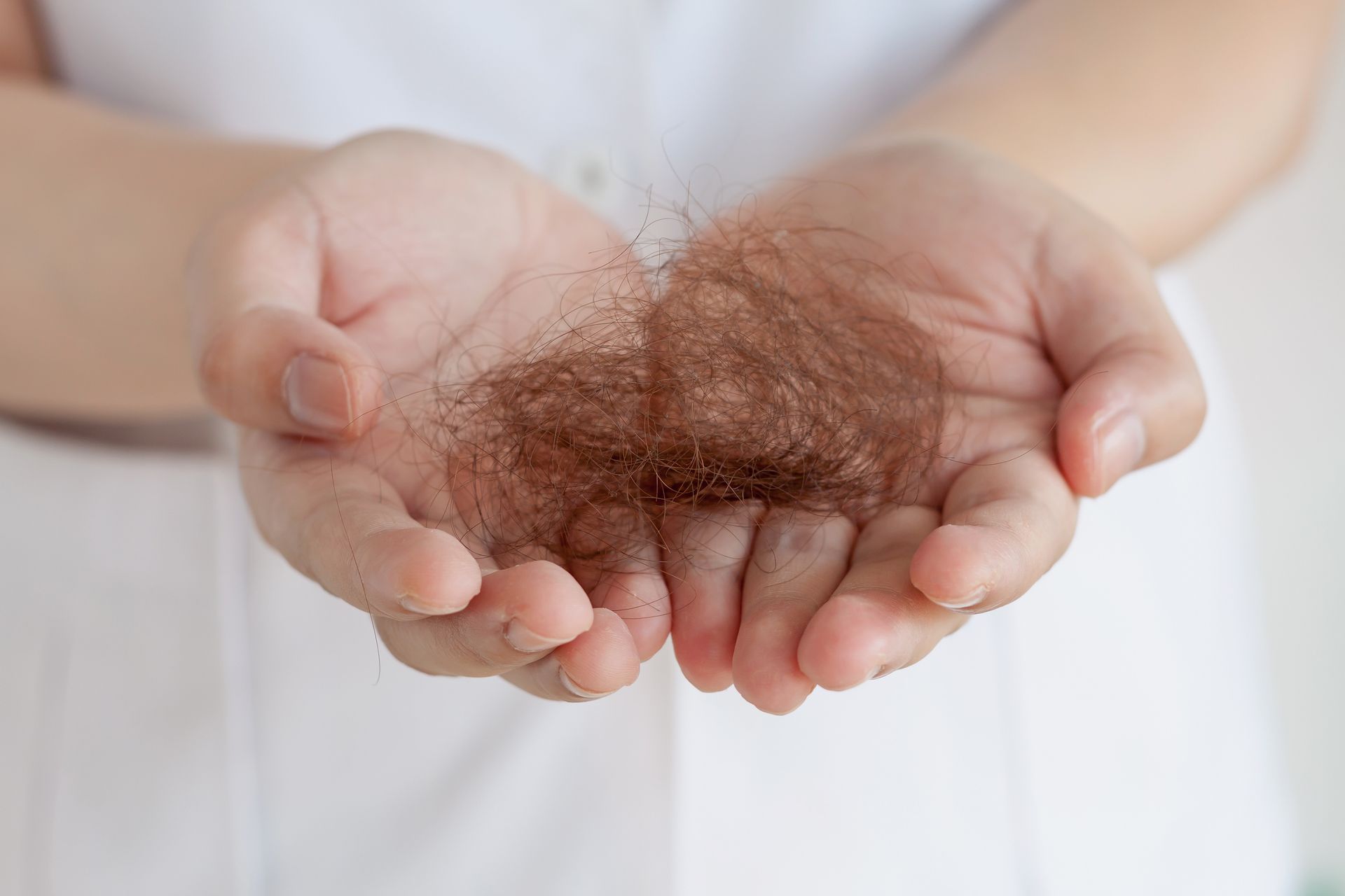 Hands holding a clump of brown hair, likely experiencing hair loss.