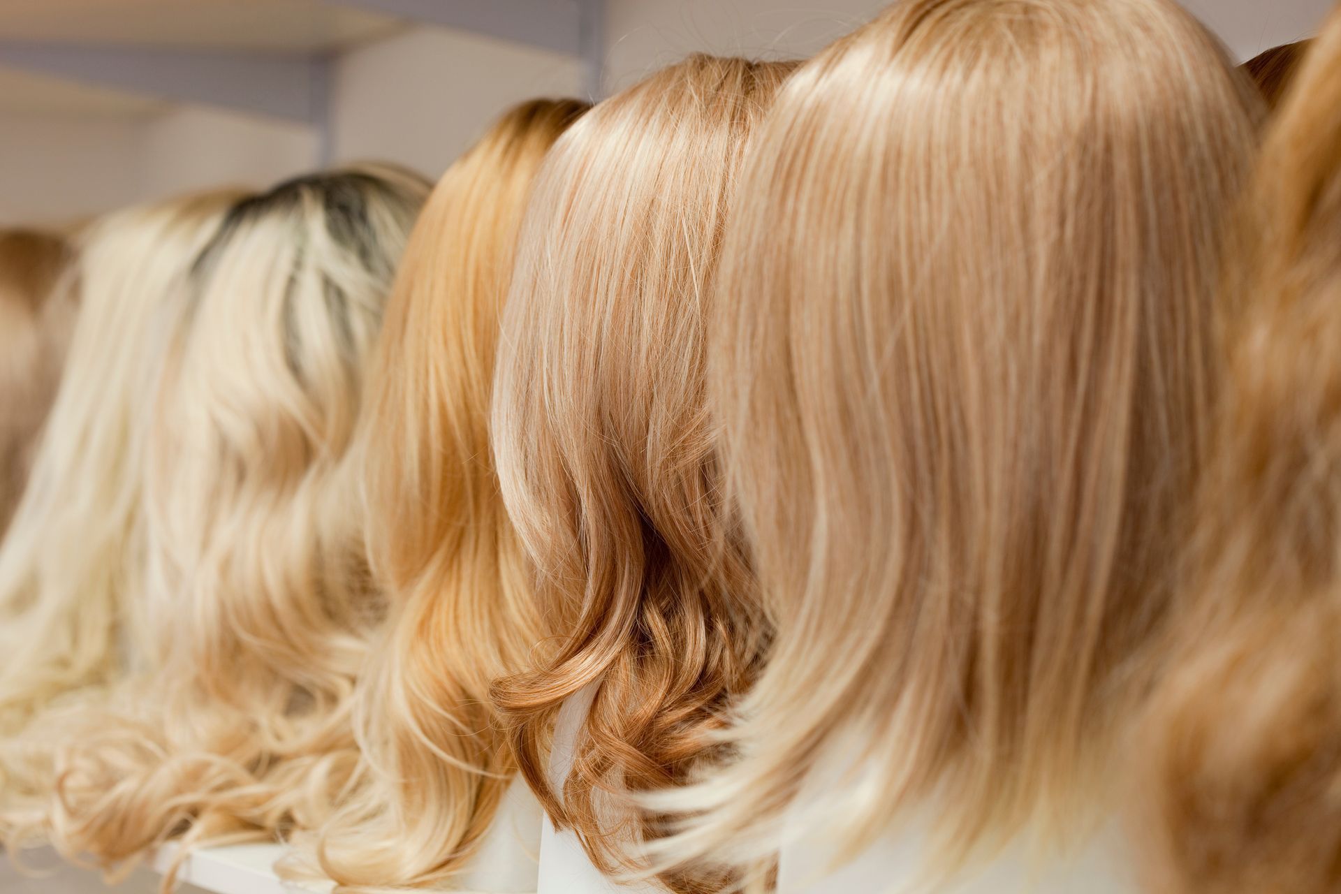 Blonde wigs on display, varying shades and styles, lined up on a shelf in a store.