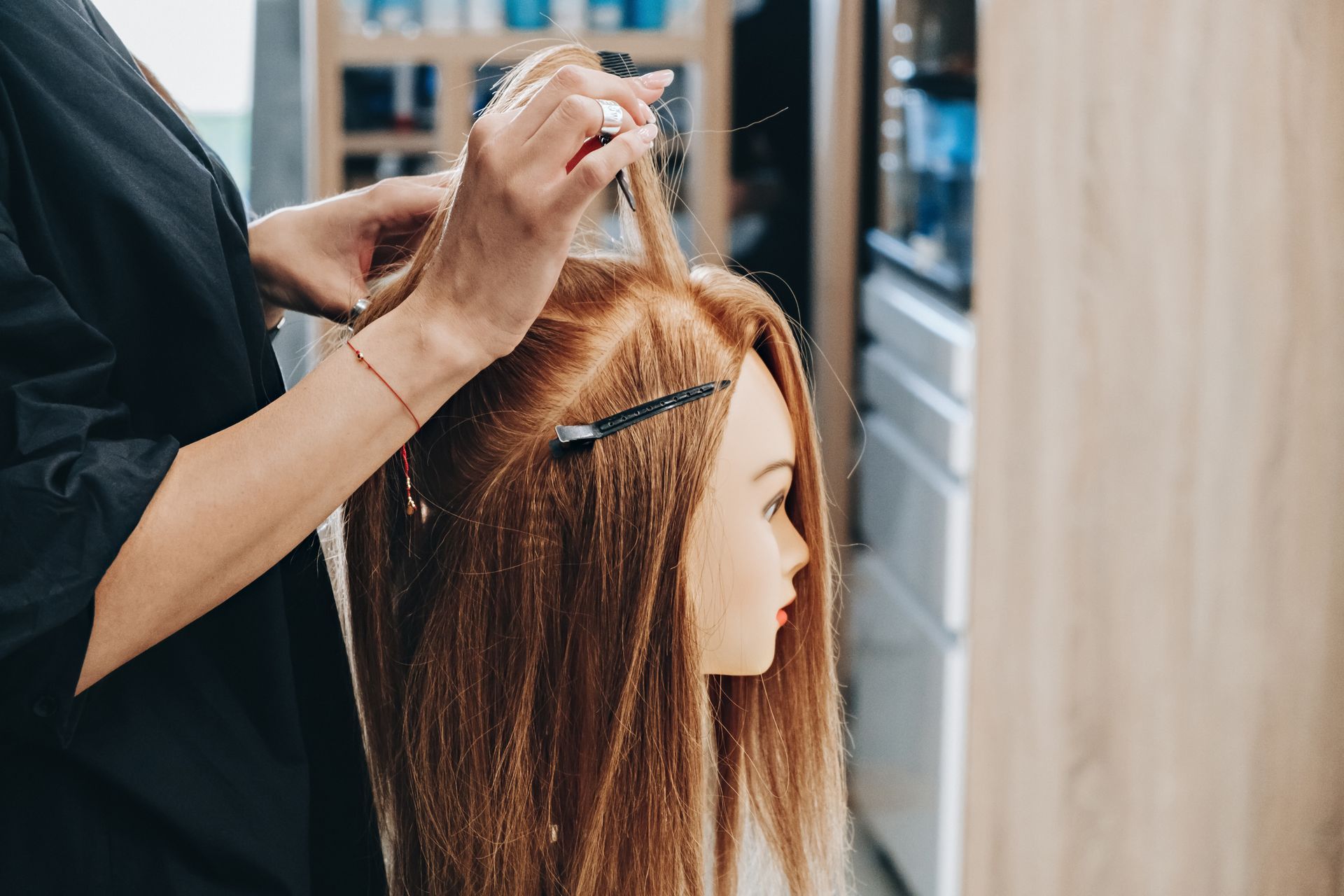 A person styling a mannequin's long, light brown hair in a salon setting.