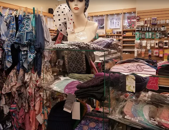 Makeup and hats on display in a store. Shelves hold lipsticks, compacts, and various colored hats.
