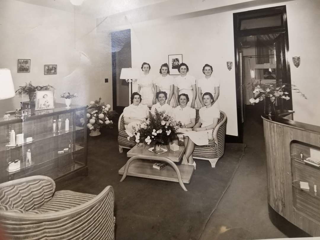 Wig shop window display: mannequins wearing various wigs on white pillars. Interior with more wigs visible.