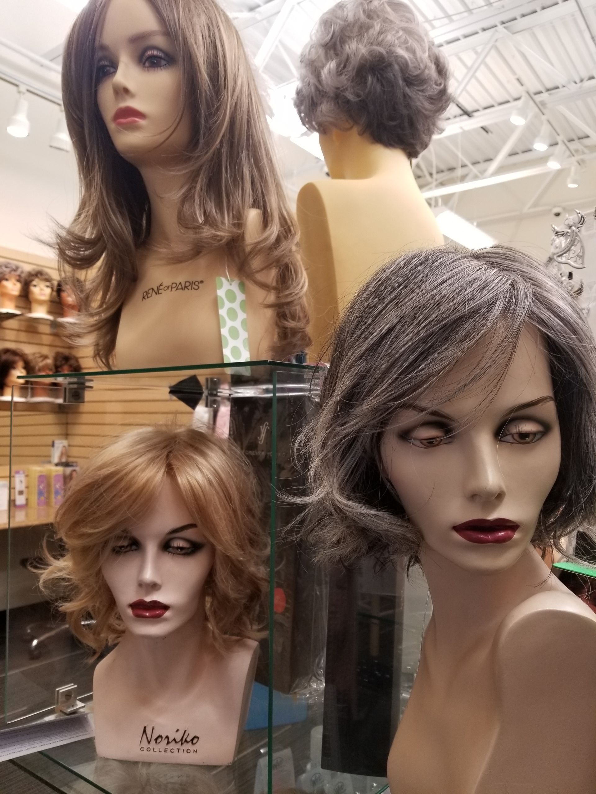 Woman in a turquoise wig poses in front of a shelf of wig displays.