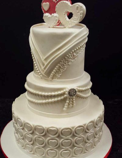 A white wedding cake with hearts and pearls on top
