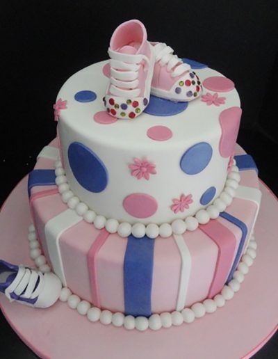 A pink and white cake with a pair of baby shoes on top