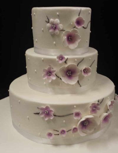 A white cake with purple flowers and pearls on it