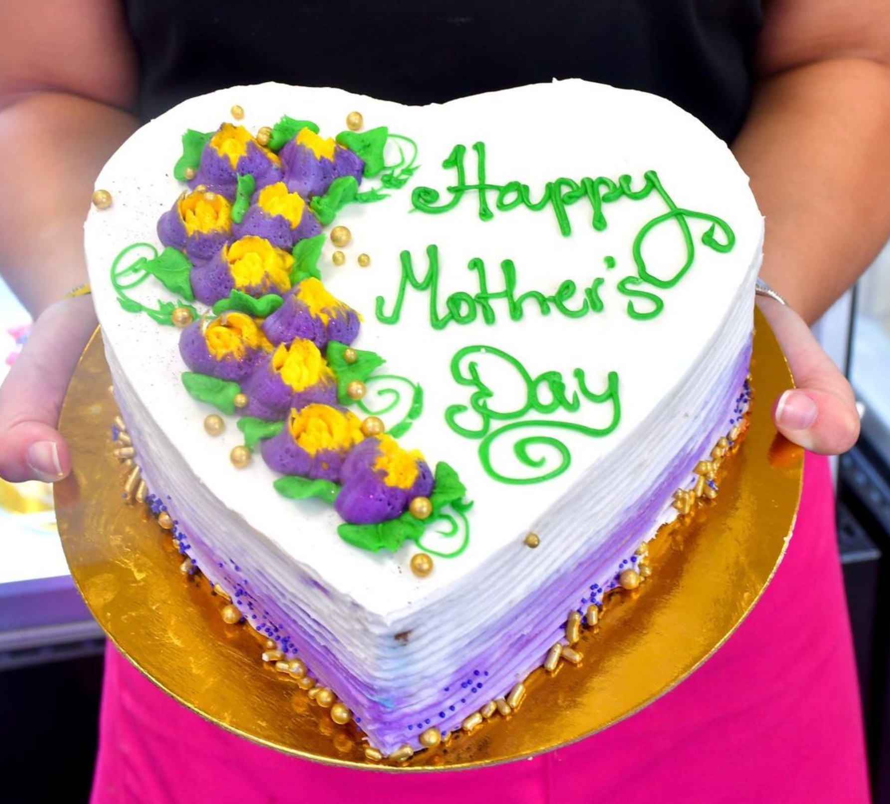 A woman is holding a heart shaped cake that says happy mother 's day