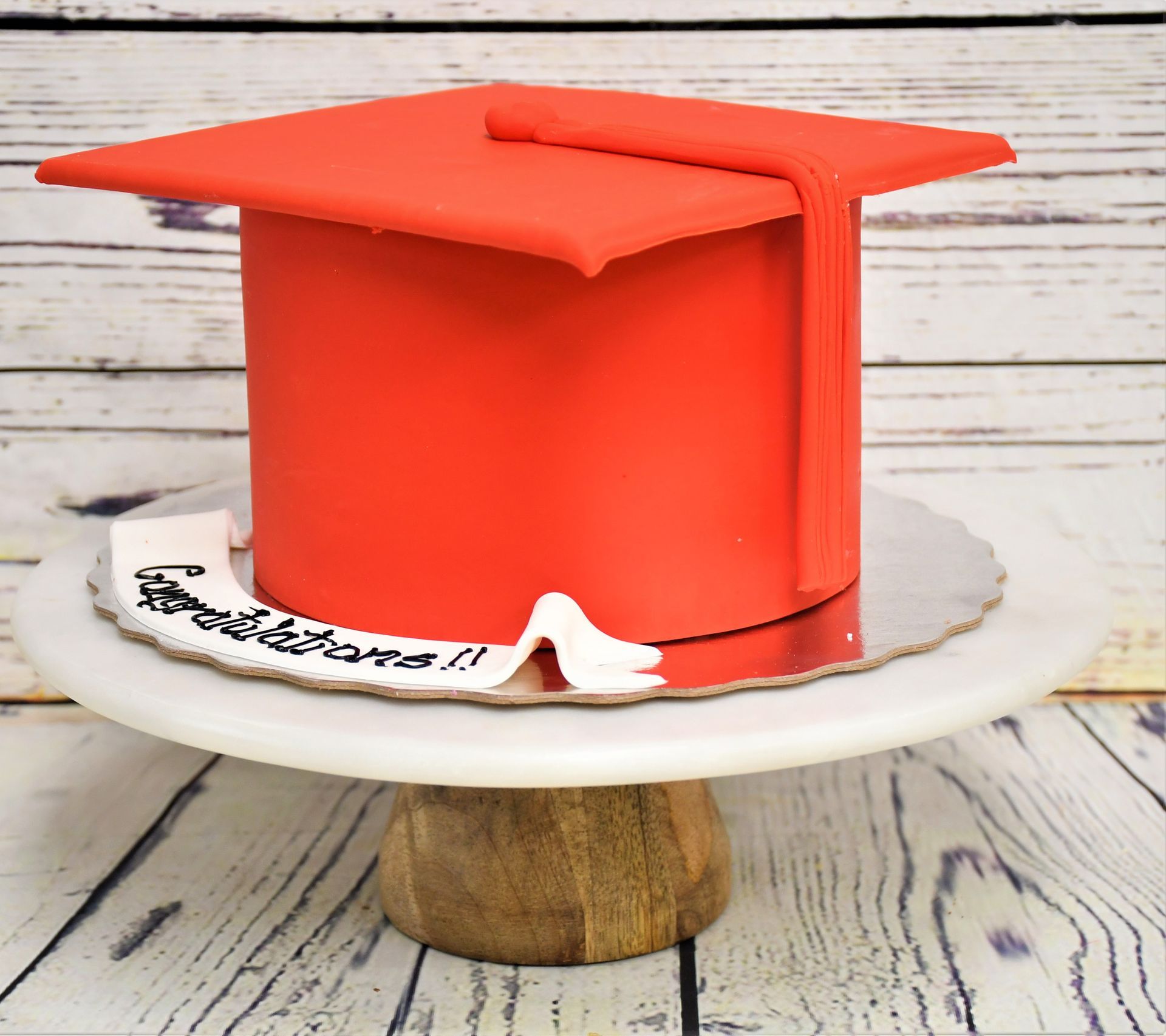 A red graduation cap cake on a white cake stand