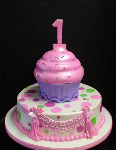 A pink and purple birthday cake with a cupcake on top