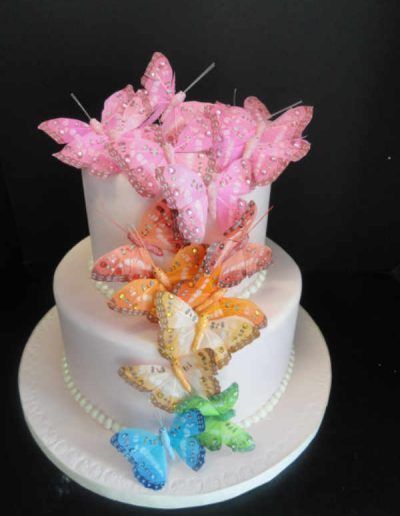 A white cake with pink butterflies and blue butterflies on it.