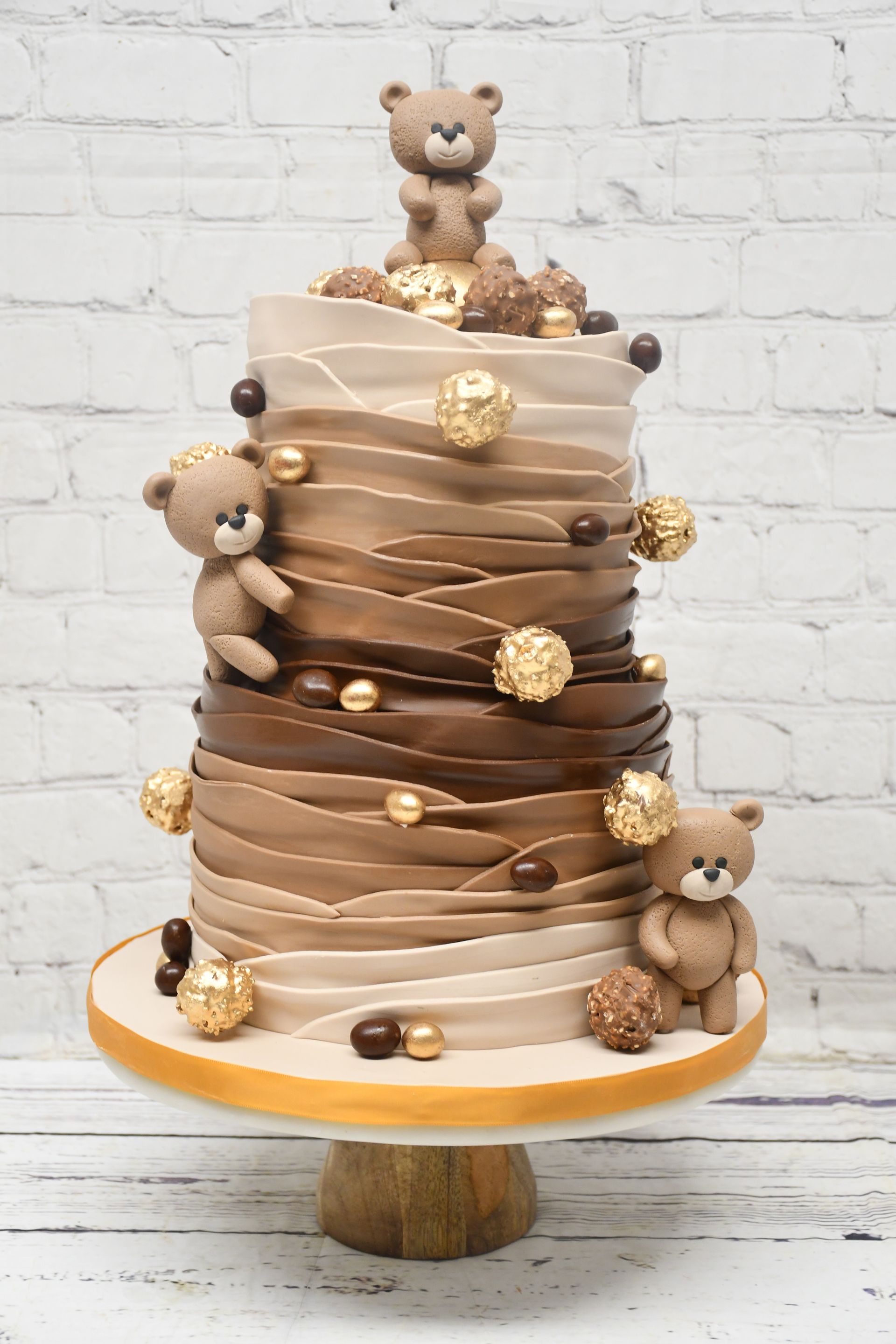 A cake with teddy bears on top of it is on a cake stand.