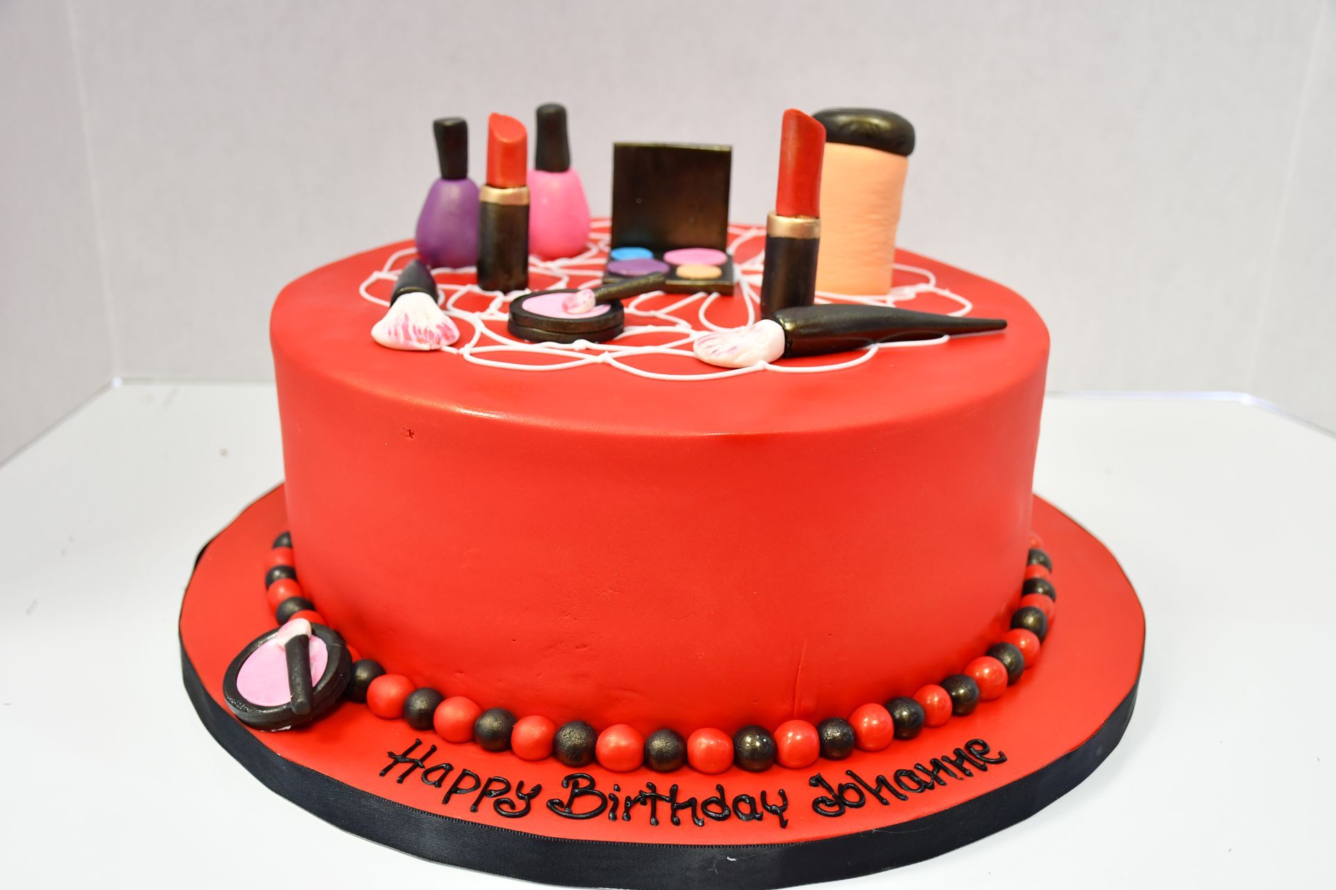 A red birthday cake with lipsticks and nail polish on it