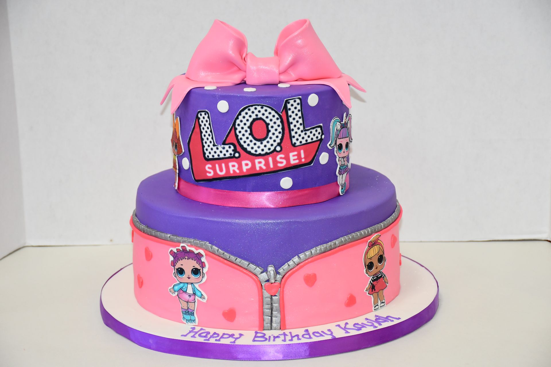 A pink and purple lol surprise cake with a pink bow