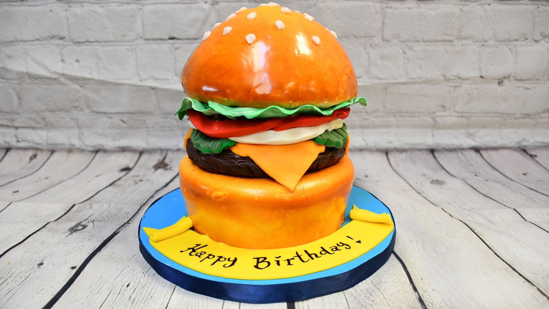 A birthday cake in the shape of a hamburger on a wooden table.