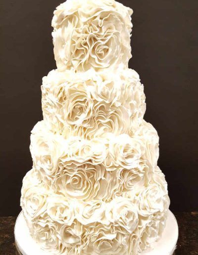 A wedding cake with white roses on it is sitting on a table.