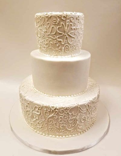 A white wedding cake with a pattern on it is sitting on a table.