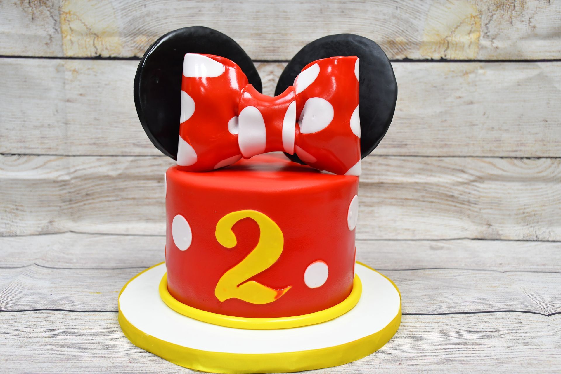 A red and yellow cake with minnie mouse ears and a bow.