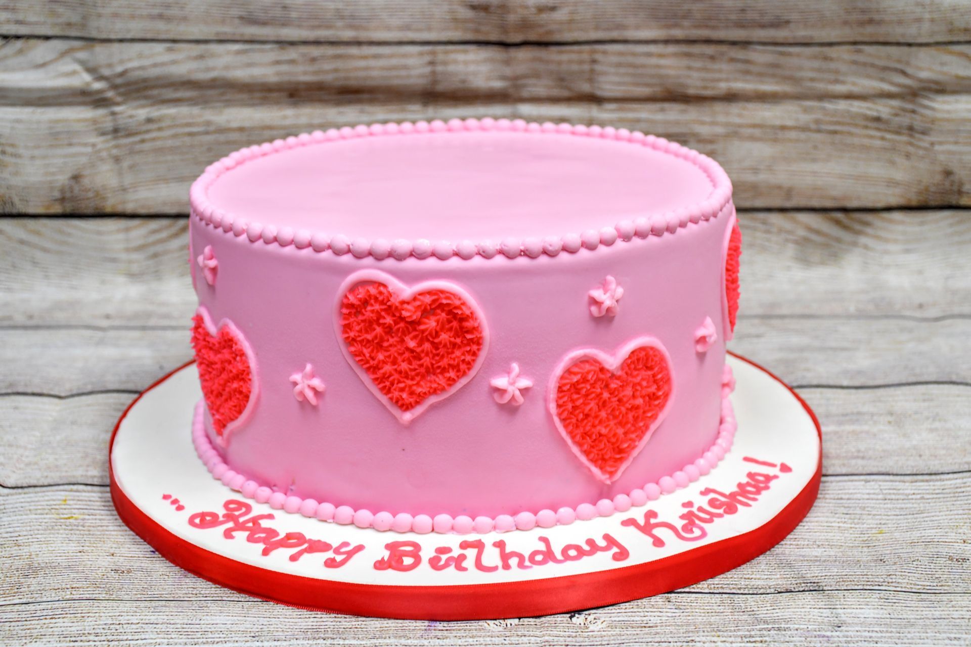 A pink birthday cake with red hearts on it