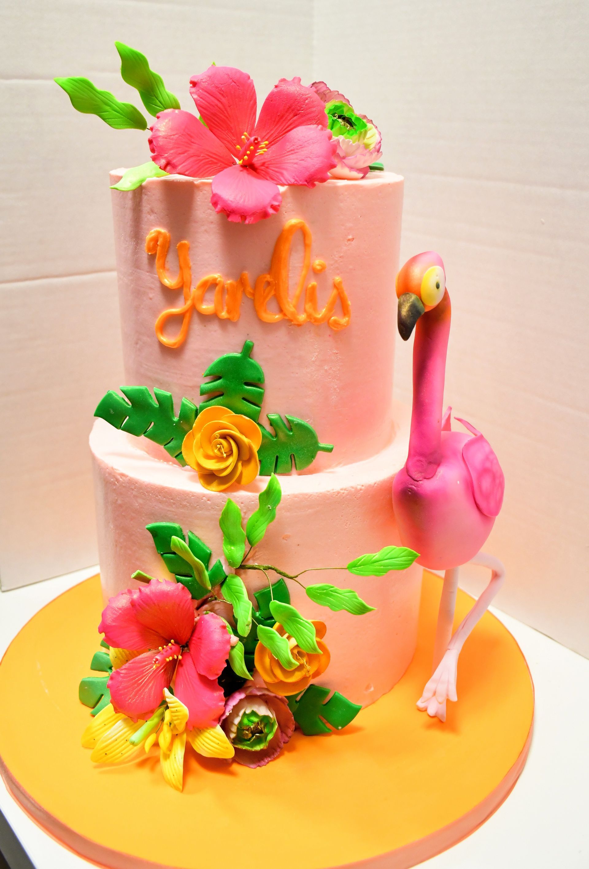 A pink cake with a flamingo and flowers on it