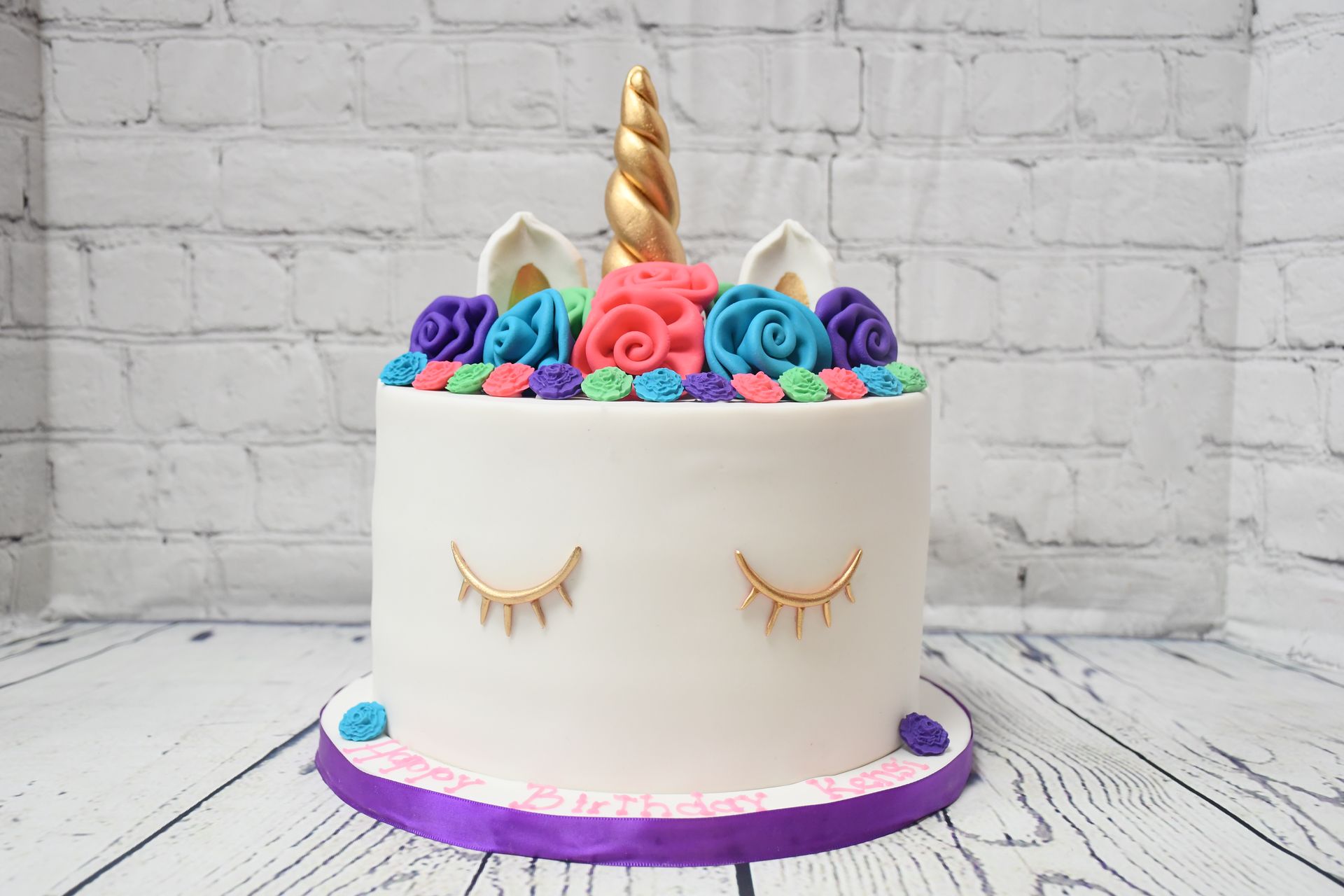 A unicorn cake with flowers on top of it is sitting on a wooden table.