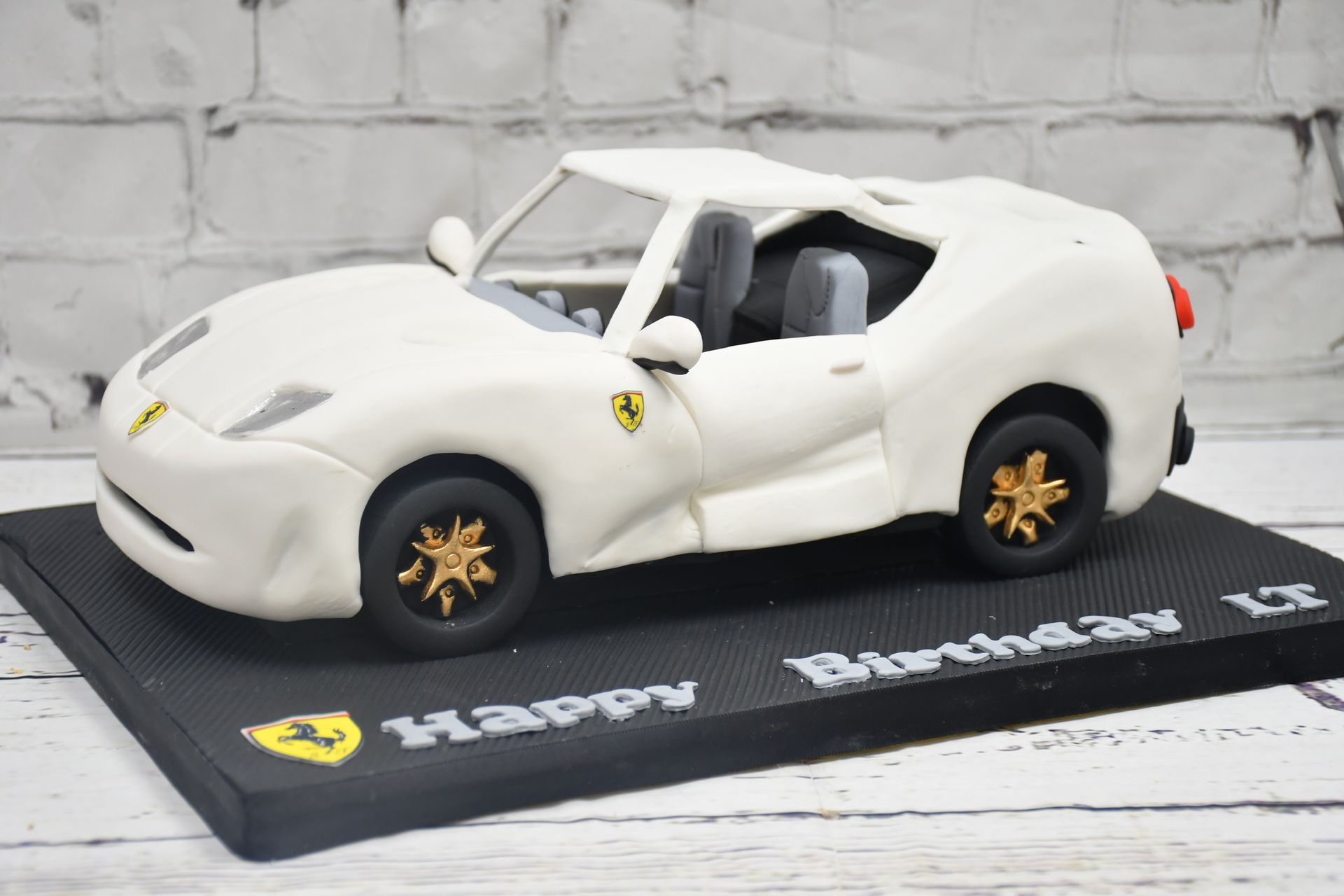 A white ferrari model car is sitting on top of a black cake.