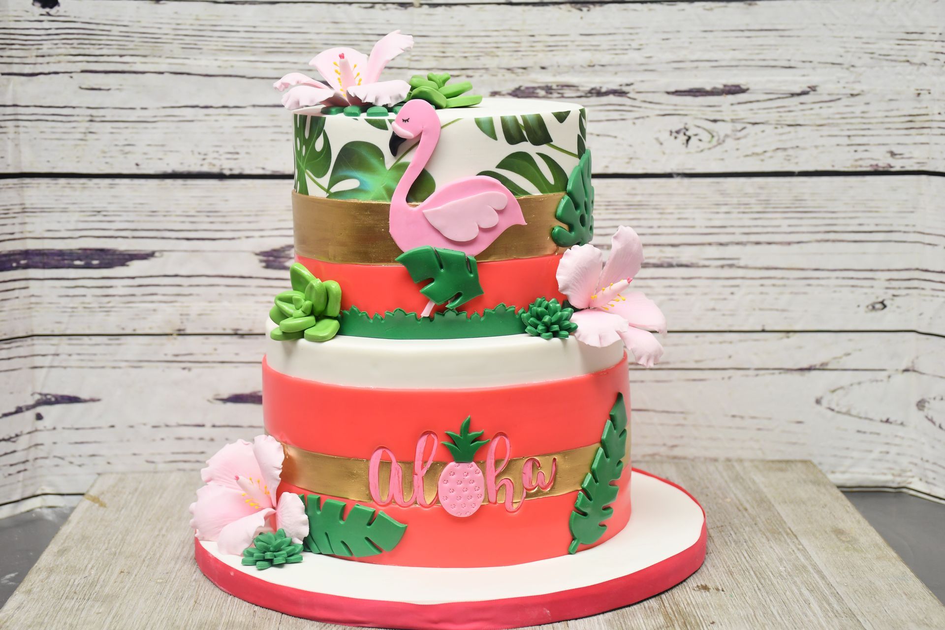 A cake with flamingos and flowers on it is sitting on a wooden table.