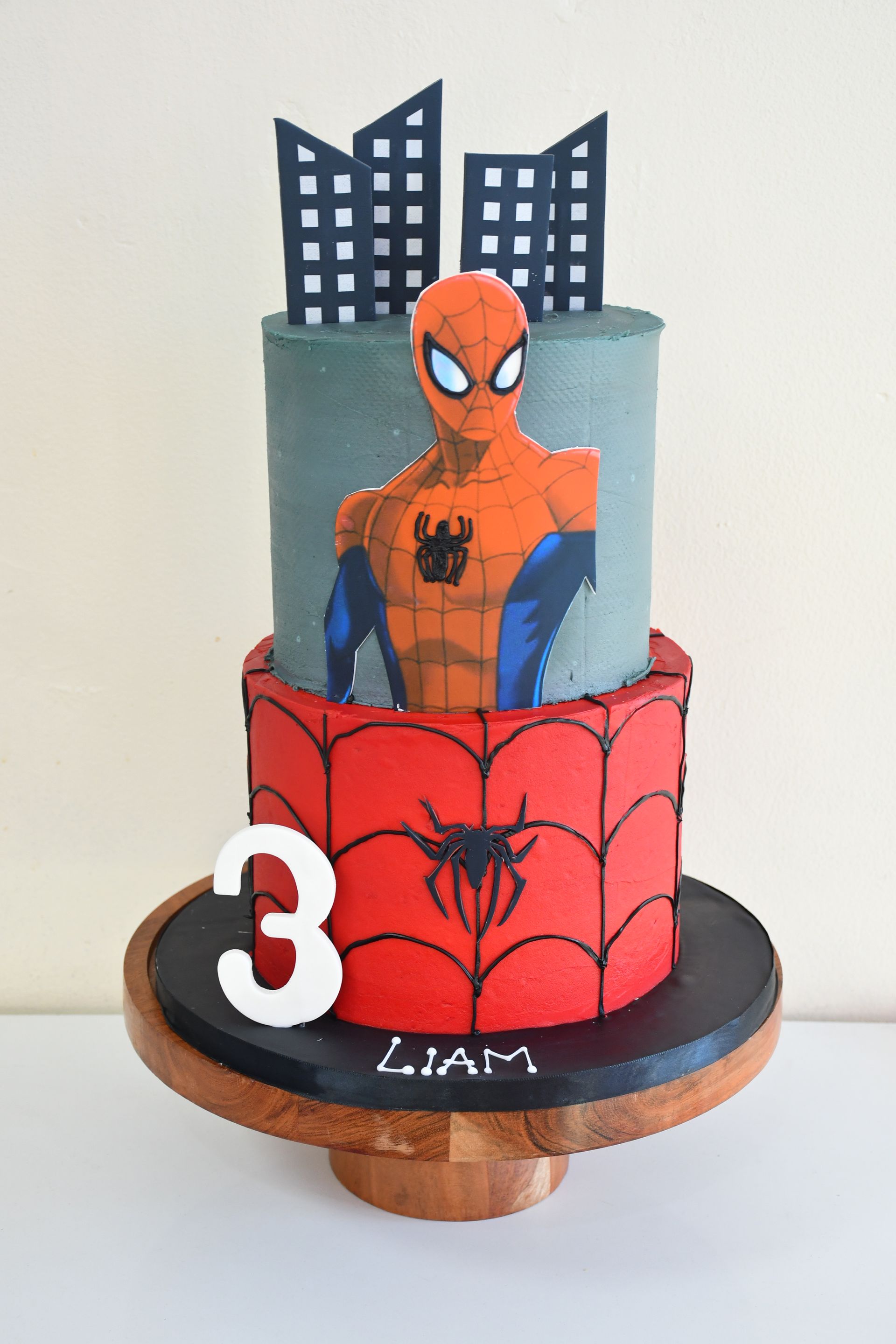 A cake with a picture of spider man on it is on a wooden stand.