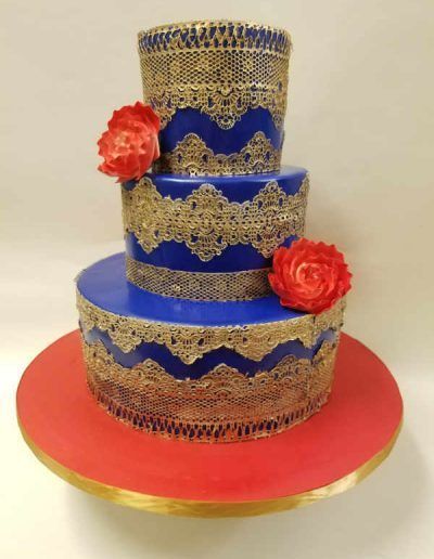 A blue and gold cake with red roses on top is on a red plate.