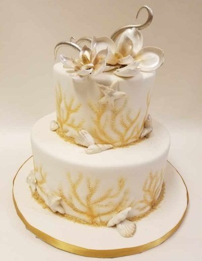 A white cake with gold flowers and seashells on it