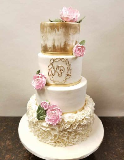 A white and gold wedding cake with pink flowers and ruffles
